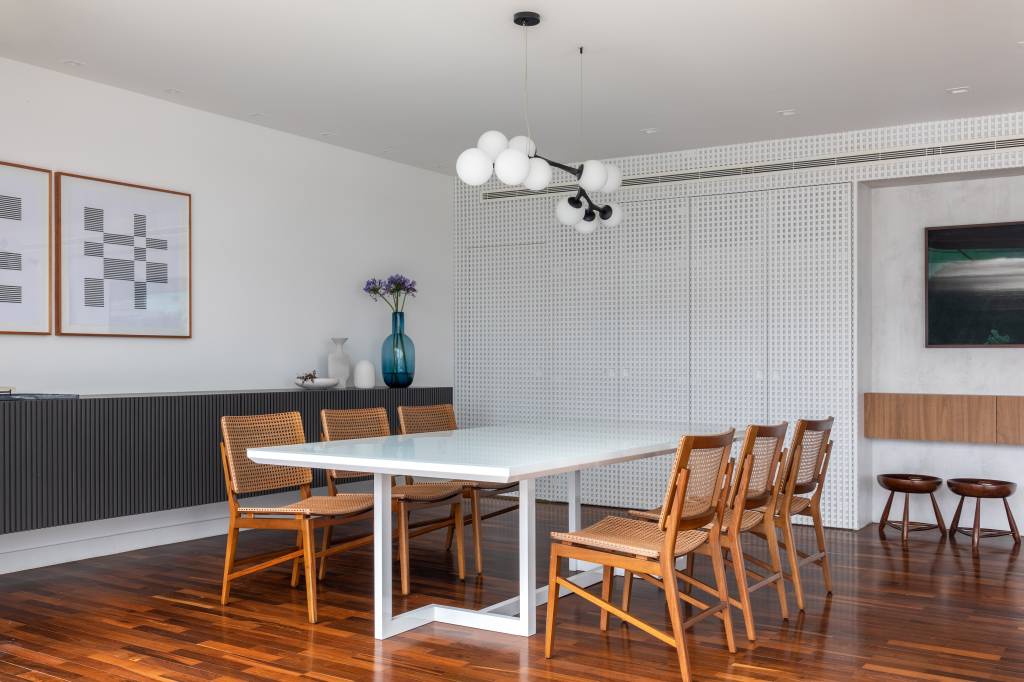 cobertura-320m-varanda-integrada-portico-muxarabi-studio-plano-arquitetura-20-jantar Sala de jantar com mesa de seis lugares branca e cadeiras de madeira.