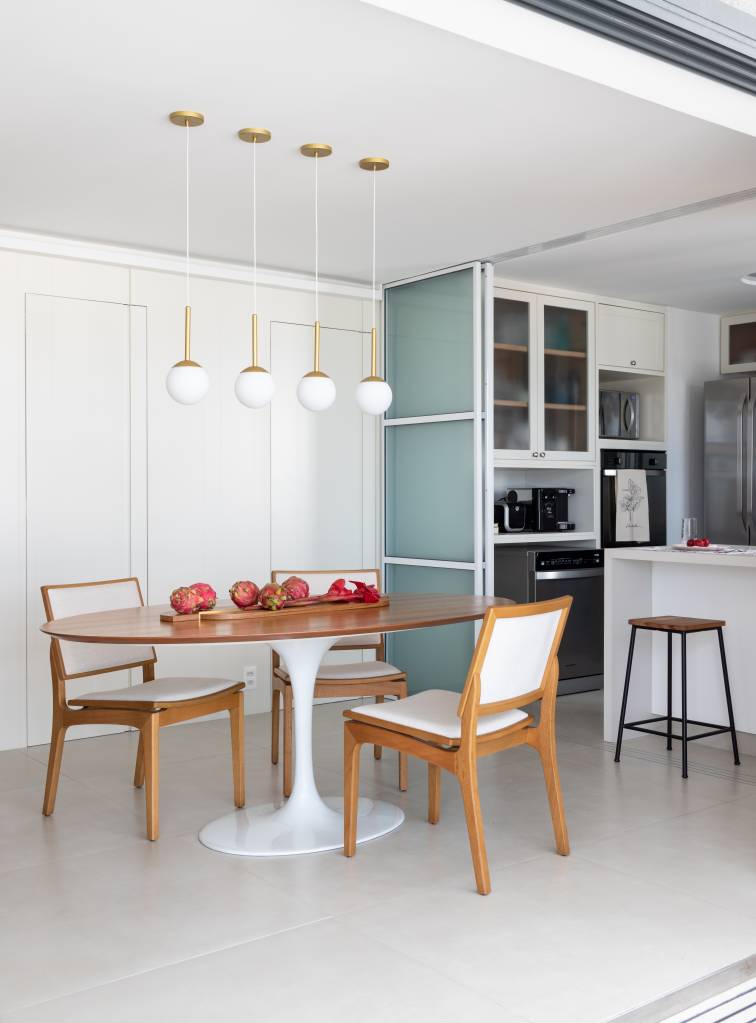 Sala de jantar com mesa redonda, piso de porcelanato e luminárias pendentes.