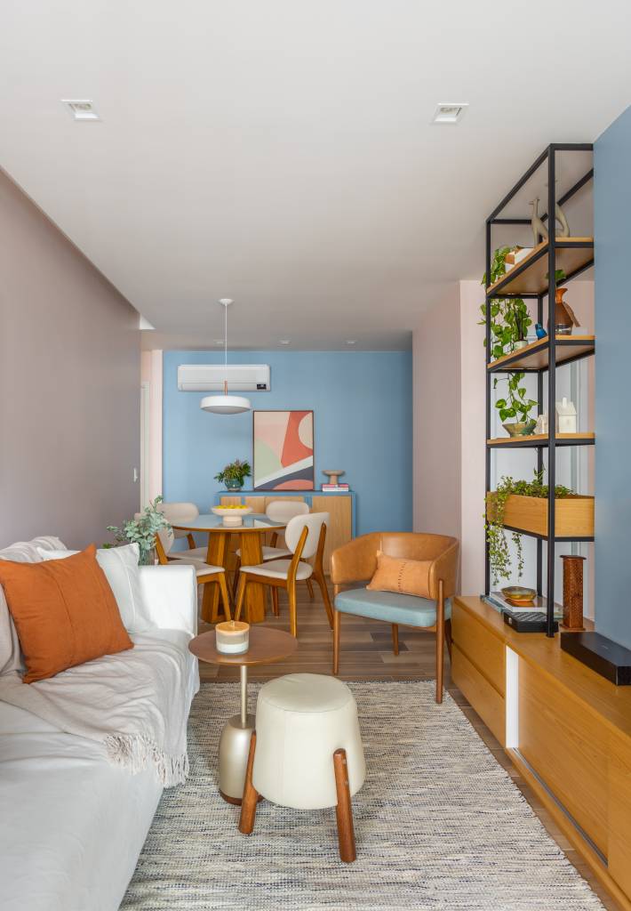 alegre-colorido-ape-80m-estante-vazada-cozinha-sala-colab-juntos-arquitetura-08-tapete-pufe Sala de estar estreita integrada com jantar; sofá claro e estante vazada.