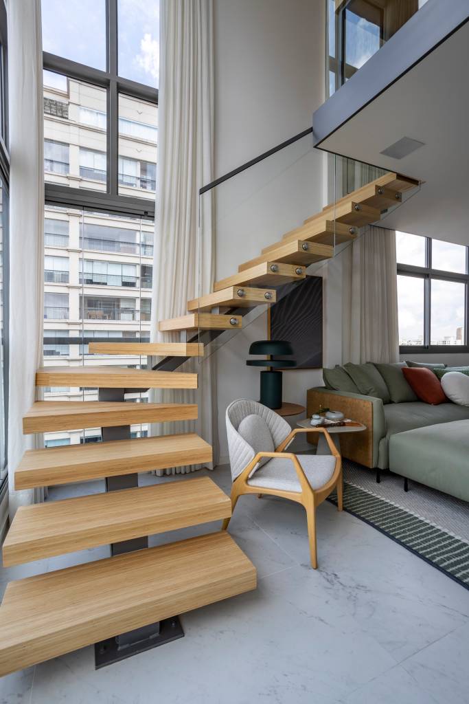 Apê de 110 m² com pé-direito duplo vira duplex com mezanino metálico Apê de 110 m² com pé-direito duplo vira duplex com mezanino metálico. Na foto, escada de madeira leva ao mezanino metálico que serve de escritório;