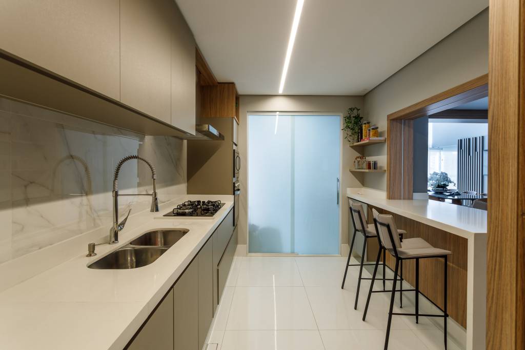 ape-180m-decoracao-neutra-pe-direito-duplo-mezanino-infinity-spaces-06 Cozinha com bancada clara, iluminação com fita de LED e marcenaria neutra.