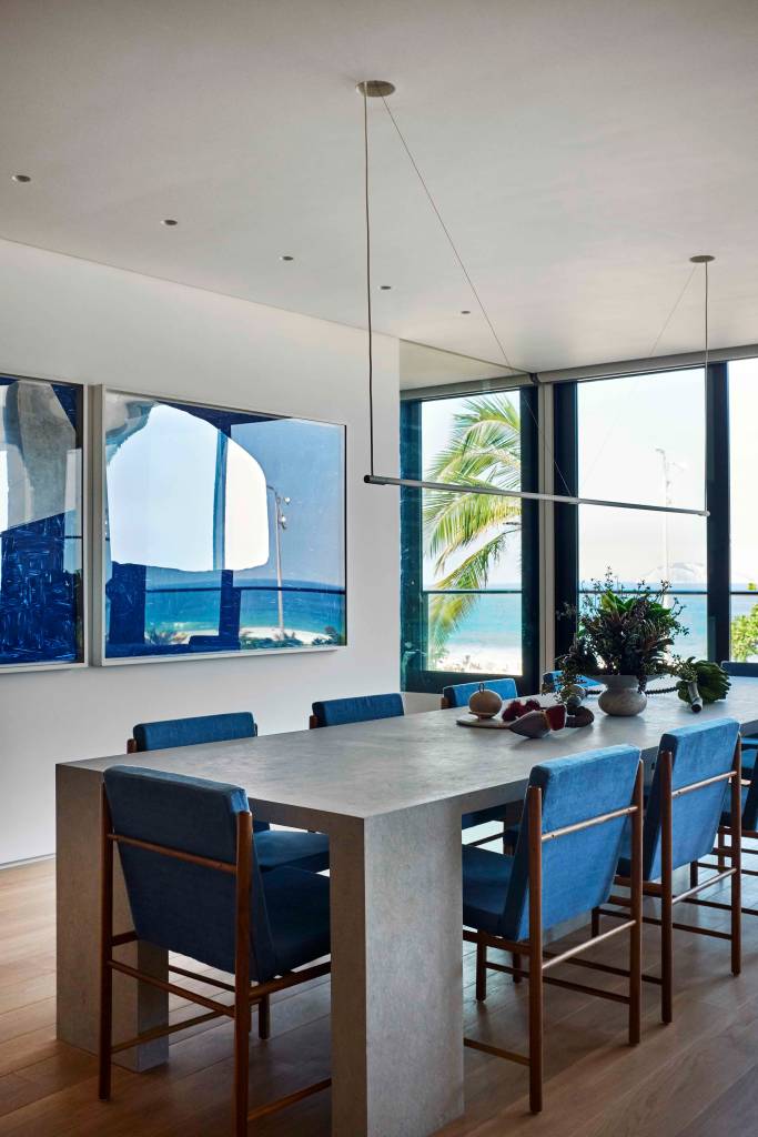 ape-350m-academia-quarto-de-hospedes-escala-arquitetura-08-jantar Sala de jantar com mesa cinza e cadeiras azuis, luminária pendente e quadros na parede.