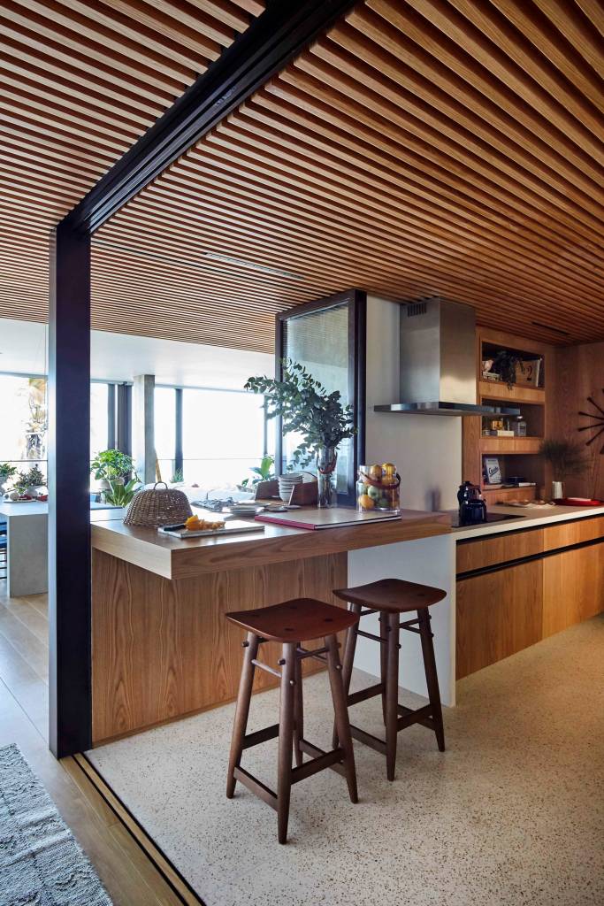 ape-350m-academia-quarto-de-hospedes-escala-arquitetura-12-cozinha-madeira Cozinha integrada com revestimentos de madeira, teto de madeira ripada, bancada de madeira com duas banquetas.