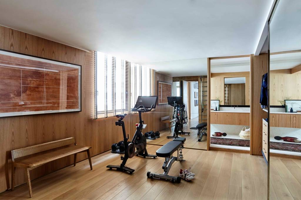 ape-350m-academia-quarto-de-hospedes-escala-arquitetura-27 Academia em casa com piso e paredes revestidas de madeira, espelho, bicicleta ergométrica e banco.