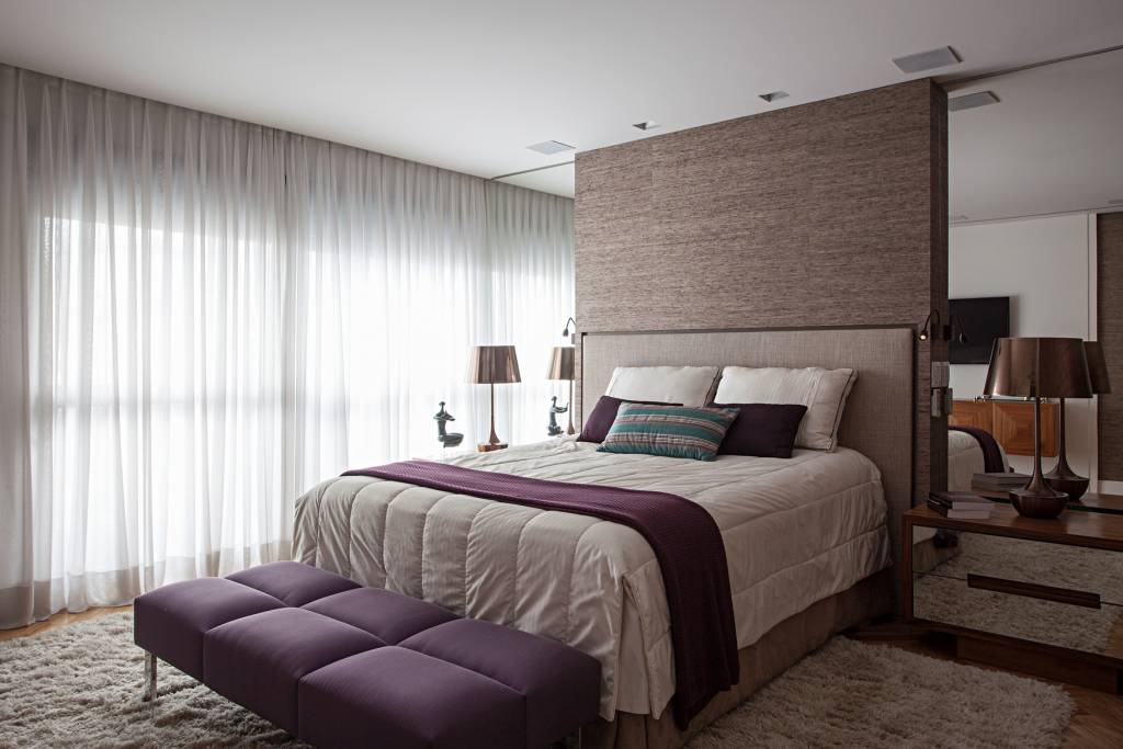 como-escolher-o-tapete-certo-korman-arquitetos-04 Quarto com tapete felpudo, cama de casal e banco roxo.