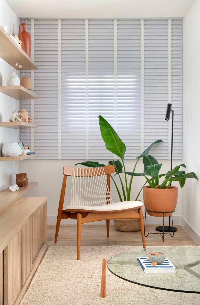 elementos-classicos-boho-branco-cobertura-210m-amanda-miranda-02-sala-persiana-cadeira-plantas Sala; cantinho de leitura com cadeira de madeira, plantas e persiana.