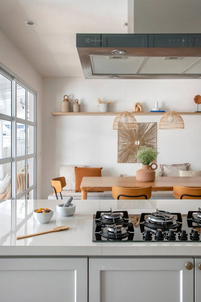elementos-classicos-boho-branco-cobertura-210m-amanda-miranda-15-cozinha Cozinha integrada; bancada branca com cooktop e sala de jantar com mesa de madeira.