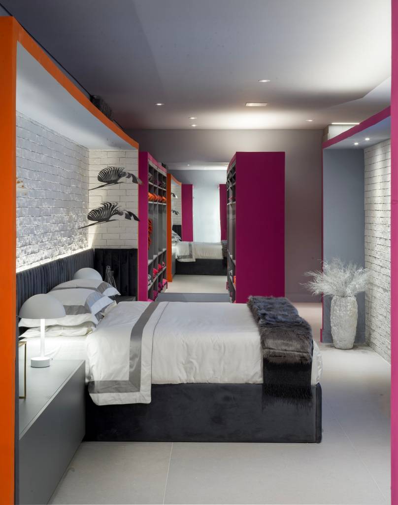 metaverso-cores-vibrantes-marcam-loft-brunete-fraccaroli-casacor-sao-paulo-2023-17 Quarto com cama de casal, cabeceira de veludo cinza e mesa lateral.