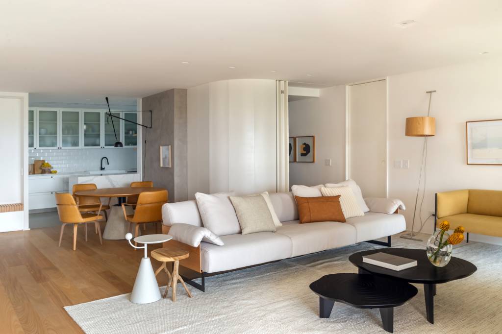 minimalista-ape-160m-varanda-integrada-formas-organicas-studio-a-g-11-sala Sala de estar com sofá branco, tapete off white, sofá em couro, mesa de centro preta.