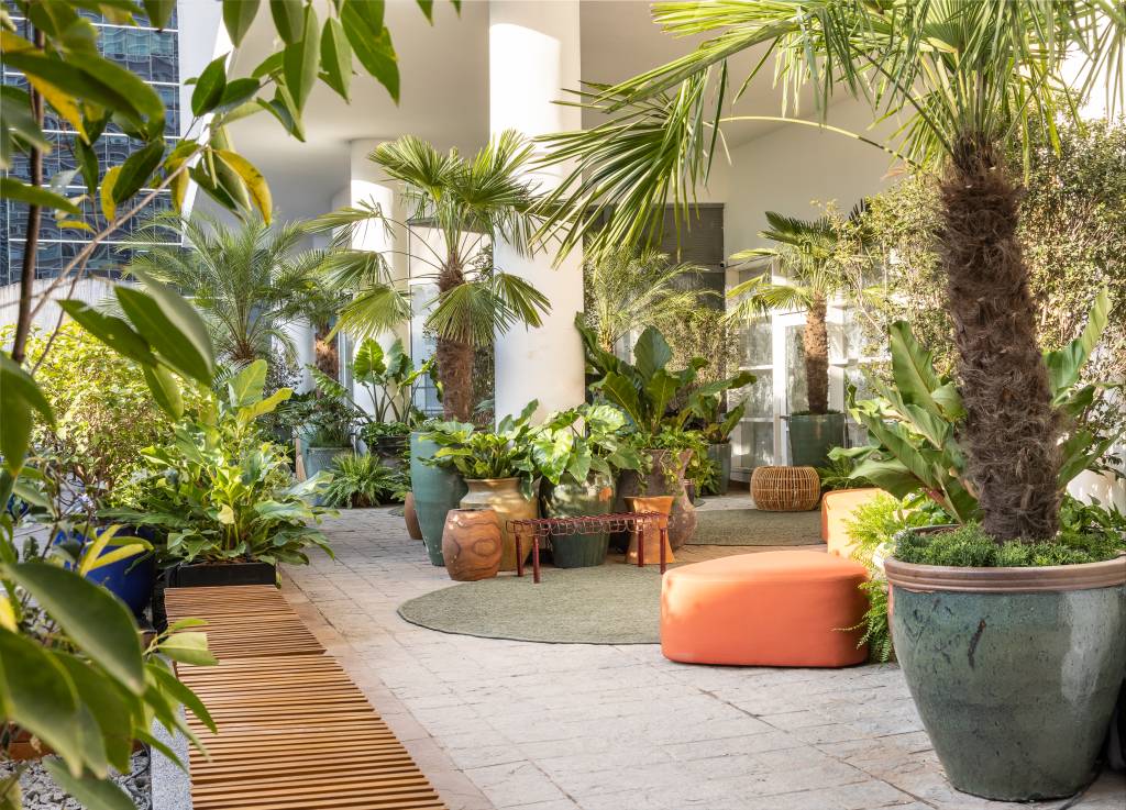 mirante-paulista-jardim-mistura-plantas-nativas-exoticas-cate-poli-e-joao-jadao-01 Jardim com vasos grandes, plantas, tapete verde e sofá curvo laranja.