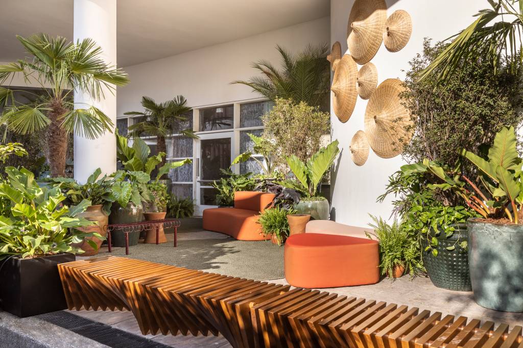mirante-paulista-jardim-mistura-plantas-nativas-exoticas-cate-poli-e-joao-jadao-02 Jardim com vasos grandes, plantas, tapete verde e sofá curvo laranja.