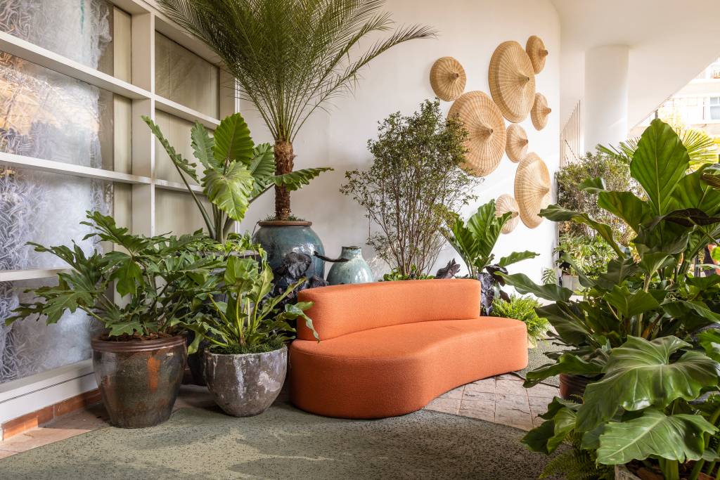 mirante-paulista-jardim-mistura-plantas-nativas-exoticas-cate-poli-e-joao-jadao-04 Jardim com vasos grandes, plantas, tapete verde e sofá curvo laranja.