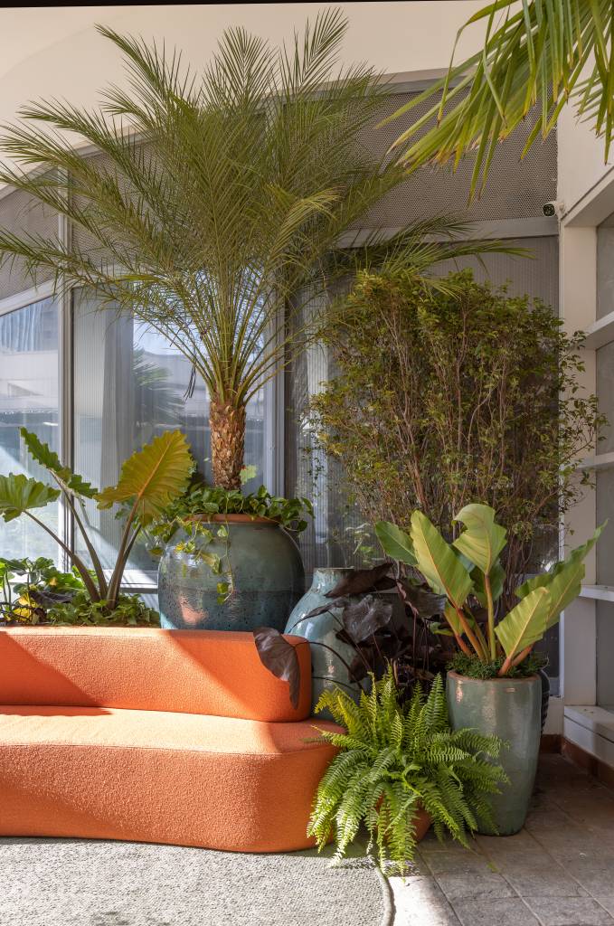 mirante-paulista-jardim-mistura-plantas-nativas-exoticas-cate-poli-e-joao-jadao-08 Jardim com vasos grandes, plantas, tapete verde e sofá curvo laranja.