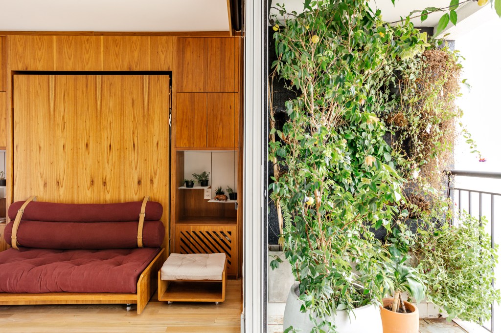 Sala com sofá vermelho e varanda pequena com jardim vertical.