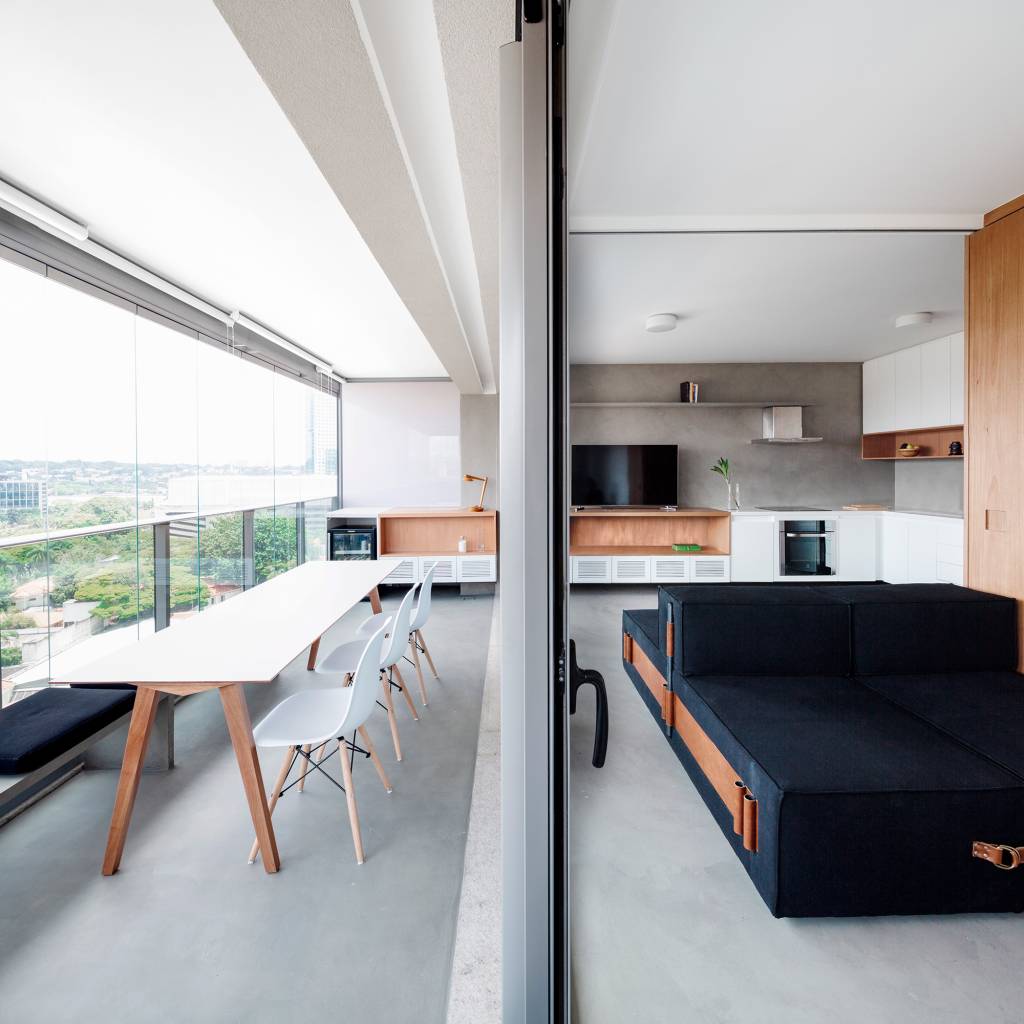 Móvel que pode ser usado como sofá, cama ou chaise setoriza apê de 64 m². Projeto VAGA Arquitetura. Na foto, sala com varanda e parede de madeira. Sofá multiuso.