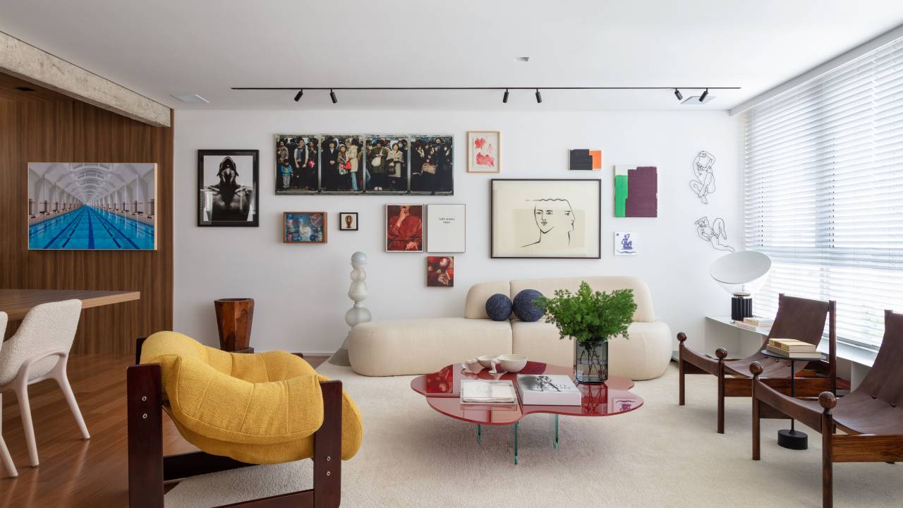 Sala de estar com tapete off white, sofá curvo, poltrona amarela, mesa de centro vermelha e quadros atrás do sofá.