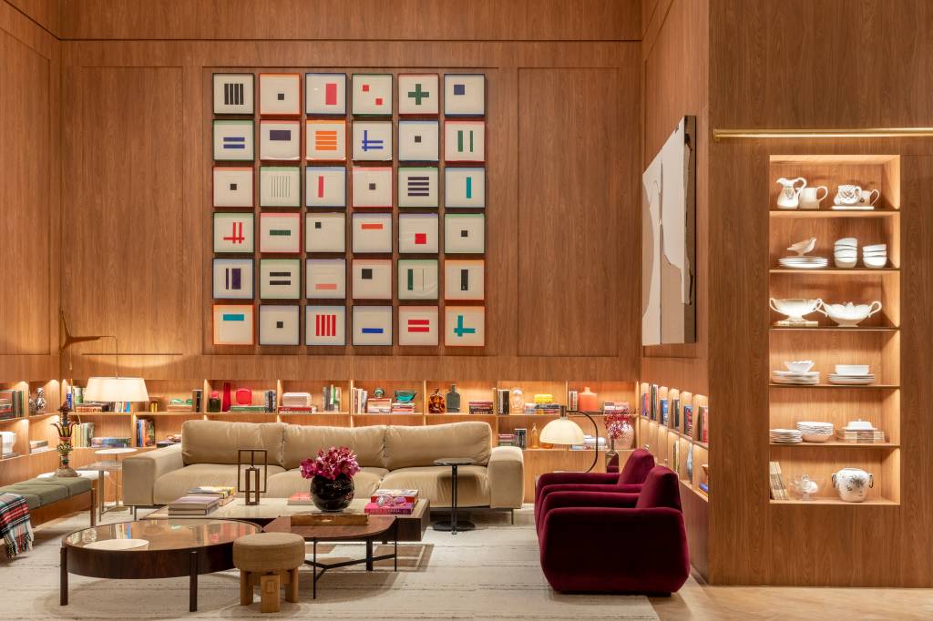 Sala de estar em madeira com sofá baixo, quadros acima do sofá, poltronas vermelhas, tapete bege e paredes revestidas de madeira.