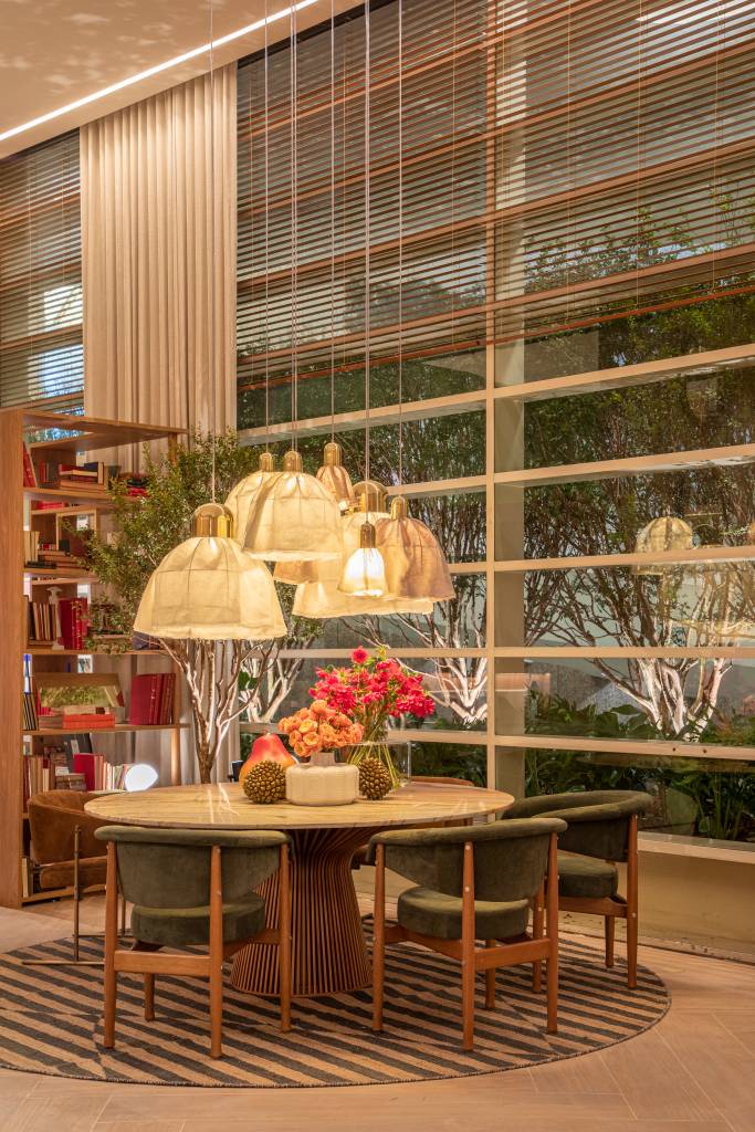 Sala de jantar com mesa redonda, cadeiras com almofadas verdes e luminárias.