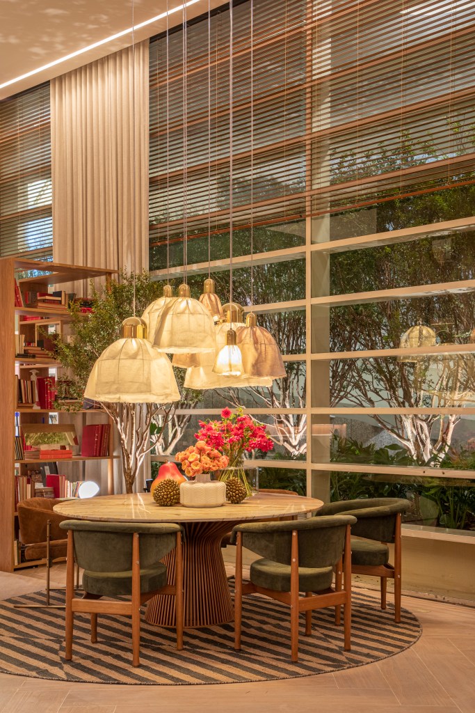 Sala de jantar com mesa redonda, cadeiras com almofadas verdes e luminárias.