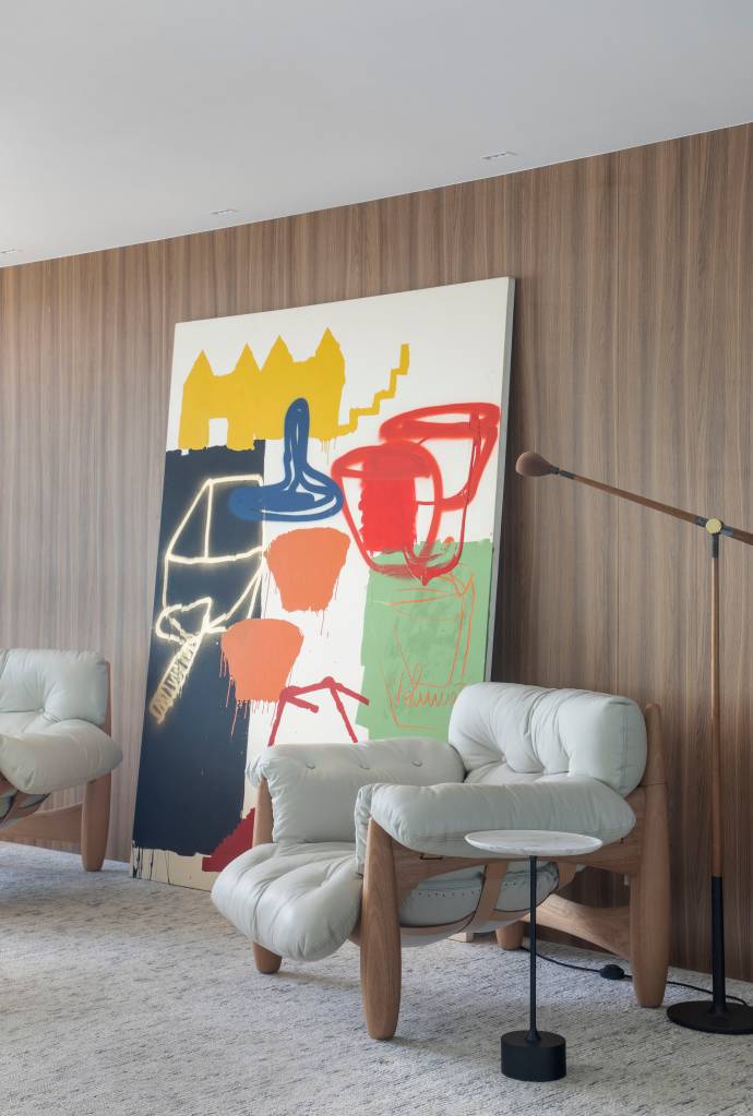 piso-marmore-branco-paineis-espelhados-ape-200m-ana-moura-ana-higino-10-sala-poltrona-quadro Sala com piso de mármore, poltrona mole branca, parede revestida de madeira e quadro.