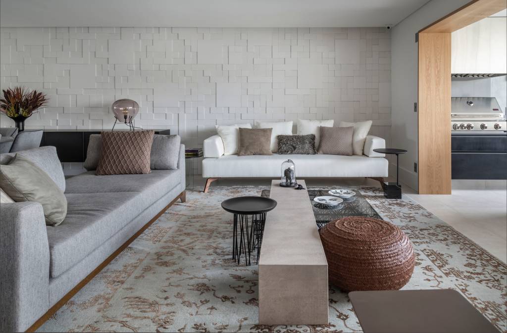 porcelanato-revestimentos-cimenticios-tons-neutros-ape-260m-renata-spinelli-06 Sala de estar com tons neutros, parede com revestimento 3d branco, tapete e sofá branco.