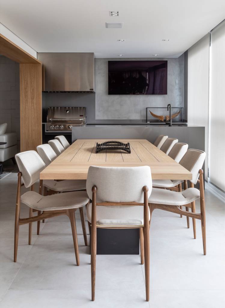 porcelanato-revestimentos-cimenticios-tons-neutros-ape-260m-renata-spinelli-07 Varanda integrada com área gourmet; mesa de madeira grande, bancada com pia e churrasqueira.