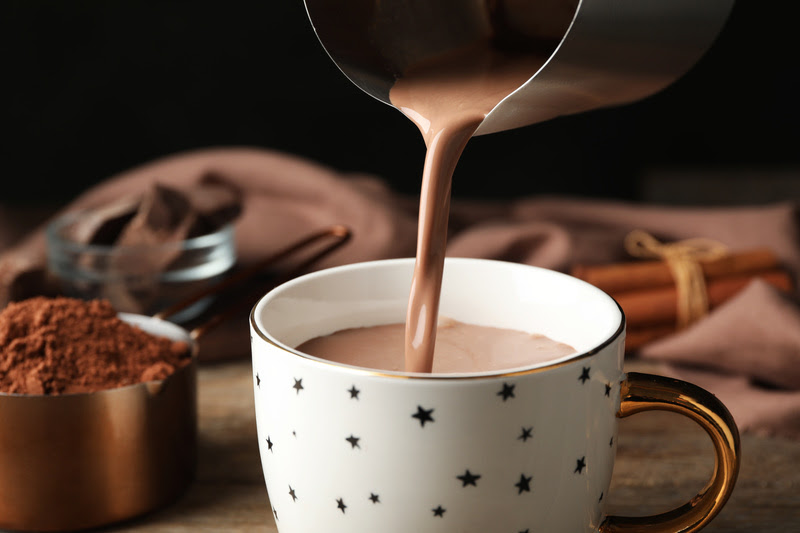 Pouring hot cocoa drink into cup on wooden table Xícara com chocolate quente.