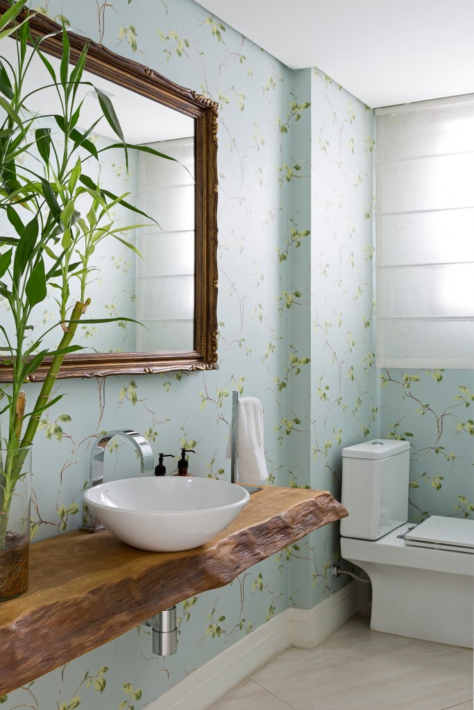 Lavabo com papel de parede e bancada rústica de madeira com cuba solta.