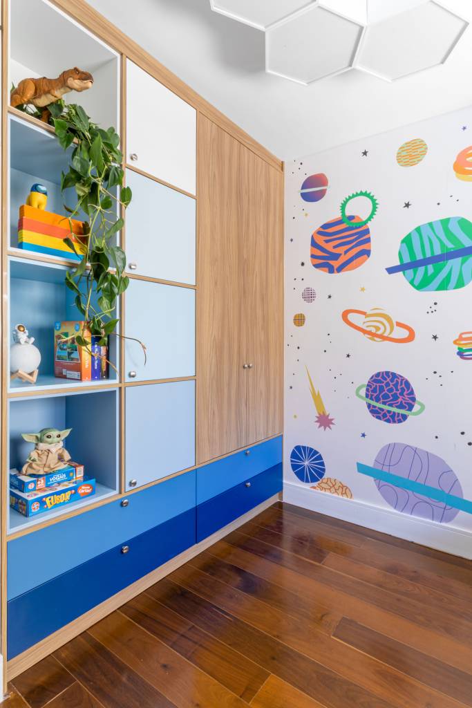 Quarto infantil com cama em caixa de madeira, parede com desenhos de planetas.