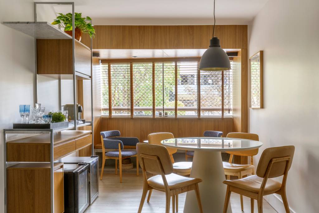 Sala de jantar pequena com mesa redonda branca, cadeiras de madeira e móvel bar.