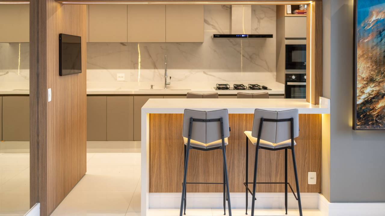 Cozinha integrada com bancada branca e banquetas de madeira.