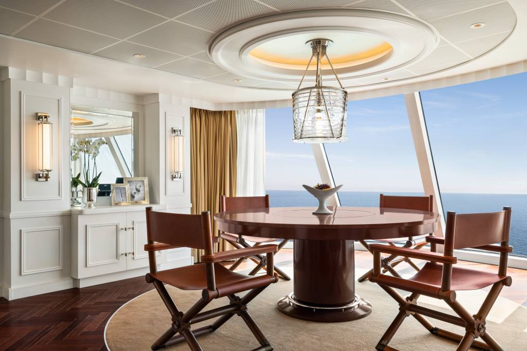 Sala de jantar com mesa redonda de madeira e parede de vidro em forma de arco.