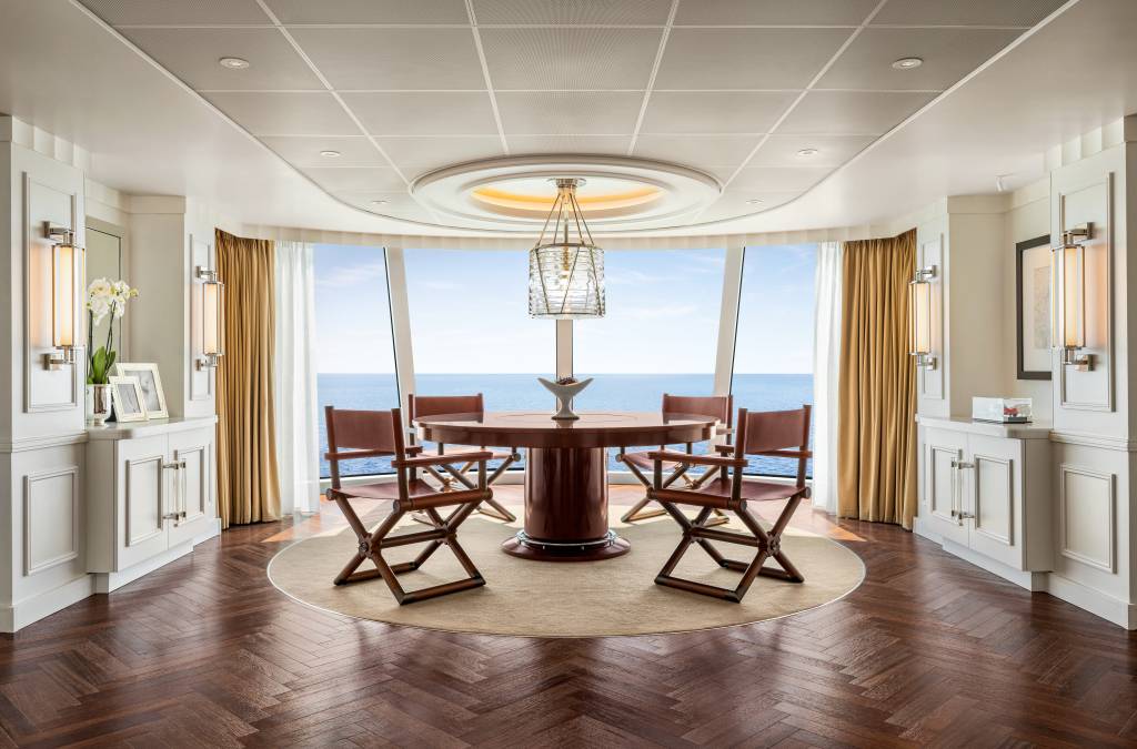 Sala de jantar com mesa redonda de madeira e parede de vidro em forma de arco.