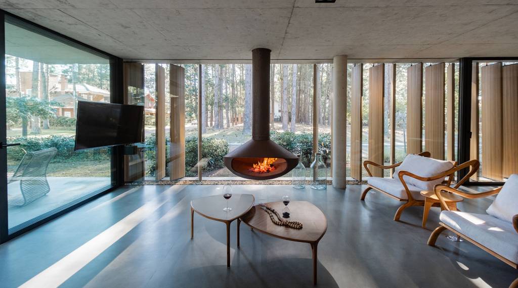 Layout minimalista marca casa térrea de 201 m² no Rio Grande do Sul. Projeto de Stemmer Rodrigues Arquitetura. Na foto, sala de estar com parede de vidro, brise e lareira.