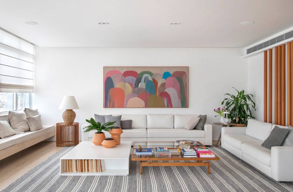 paleta-cores-claras-ripados-madeira-ape-275m-studio021arquitetura-06-sala Sala de estar branca com sofá branco, tapete listrado azul, banco branco e mesa de centro de madeira.