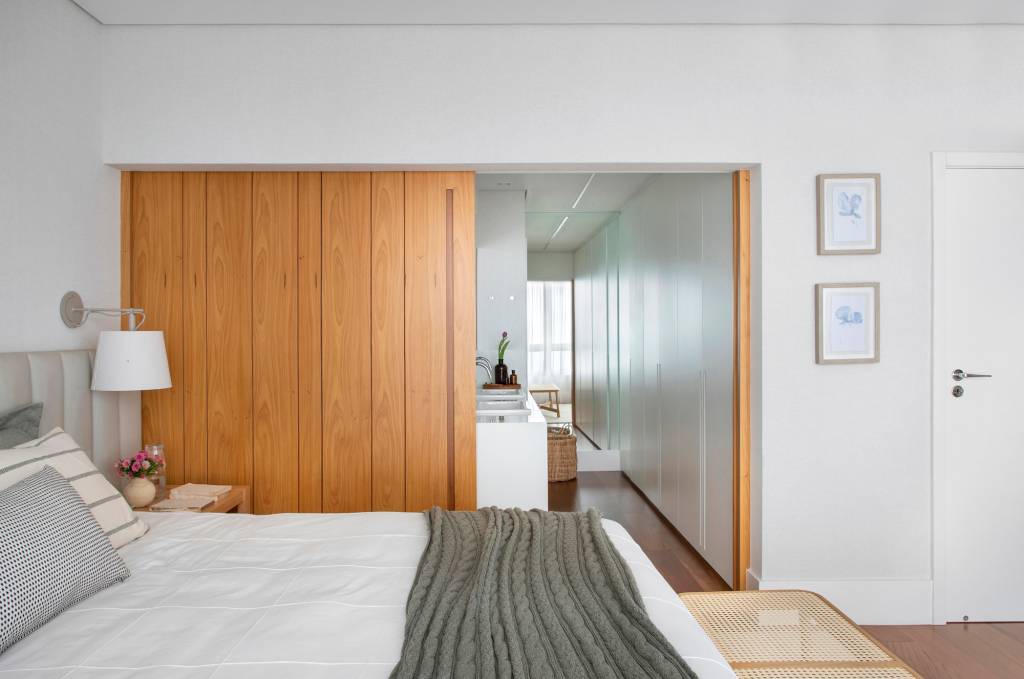 paleta-cores-claras-ripados-madeira-ape-275m-studio021arquitetura-17 Quarto; suíte com cama de casal, cabeceira estofada e banheiro e closet com porta de correr de madeira.
