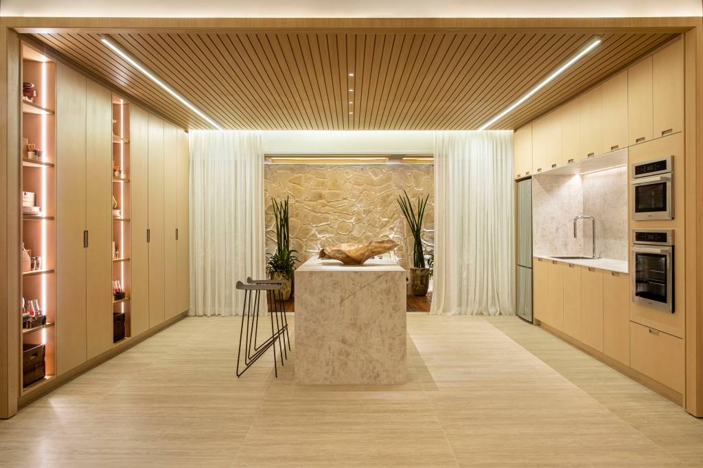 quiet-luxury-feng-shui-indiano-loft-120-m2-bianca-da-hora-credito-mca-estudio (7) Quiet luxury e feng shui indiano marcam este loft de 120 m², Projeto de Bianca Da Hora Arquitetura para a CASACOR SP 2023. Na foto, cozinha com ilha, teto ripado, armários, torre quente e parede de pedra.