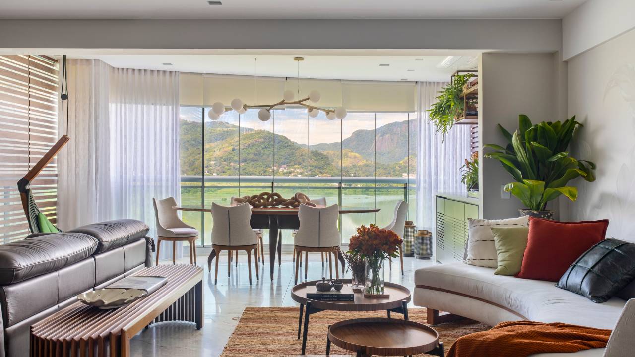 Sala de estar integrada com varanda, piso de porcelanato marmorizado, sofá curvo claro e tapete terracota;
