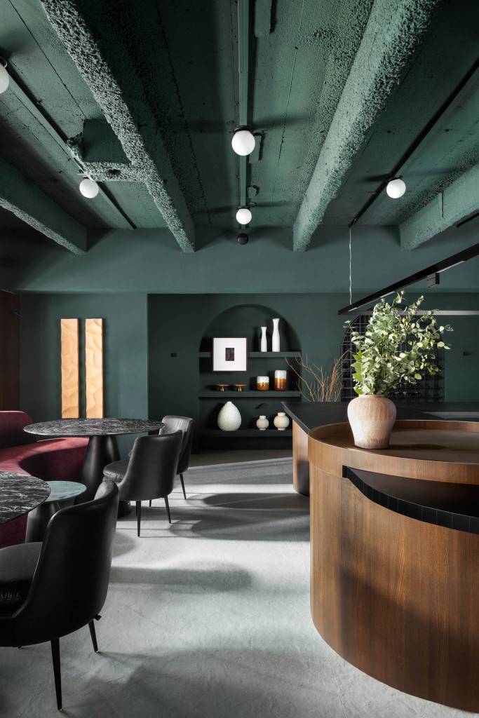 50 mil hastes de aspargos secos adornam o teto deste restaurante. Projeto de Renan Altera para a CASACOR SP 2023. Na foto, mesas de pedra, poltronas curvas e teto verde.