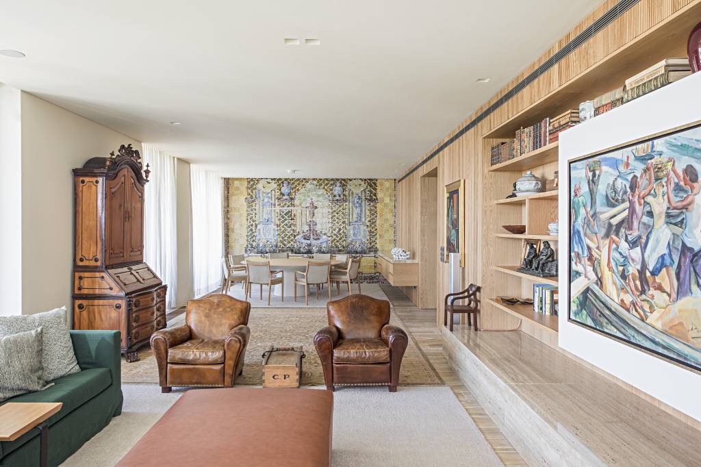 apartamento-portugal-tv-escondida-atras-quadro-deslizante-mauricio-nobrega-12 Sala de estar com estante de madeira com quadro que desliza, sofá verde, poltronas vintage de couro e tapetes.