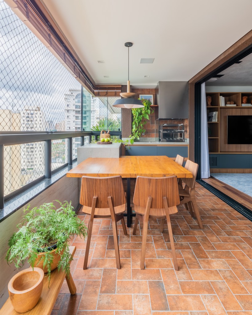 Projeto de Pietro Terlizzi. Na foto, varanda integrada gourmet com mesa de madeira e churrasqueira.