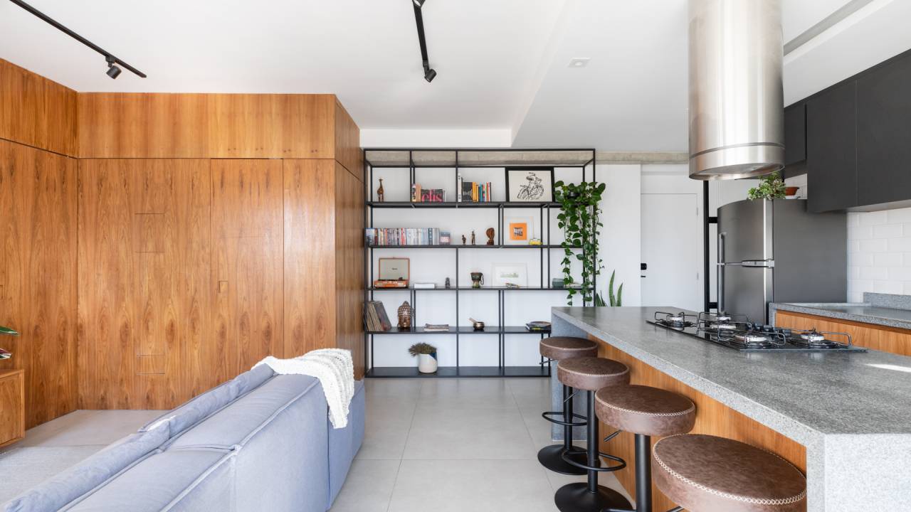 Apê de 60 m² ganha cozinha com ilha e vista para o centro de SP. Projeto de Estúdio Taco. Na foto, cozinha com ilha integrada com estar. Paredes de painel de madeira.