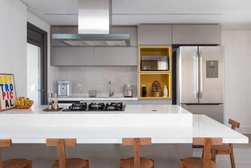 atmosfera-personalizada-apes-com-a-mesma-planta-studio-tan-gram-04 Cozinha integrada com marcenaria cinza e ilha com bancada branca e banquetas de madeira.