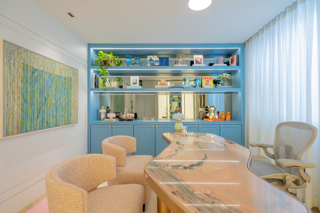 Projeto de Romário Rodrigues Arquitetos. Na foto, home office com tapete colorido, mesa de pedra e estante azul.