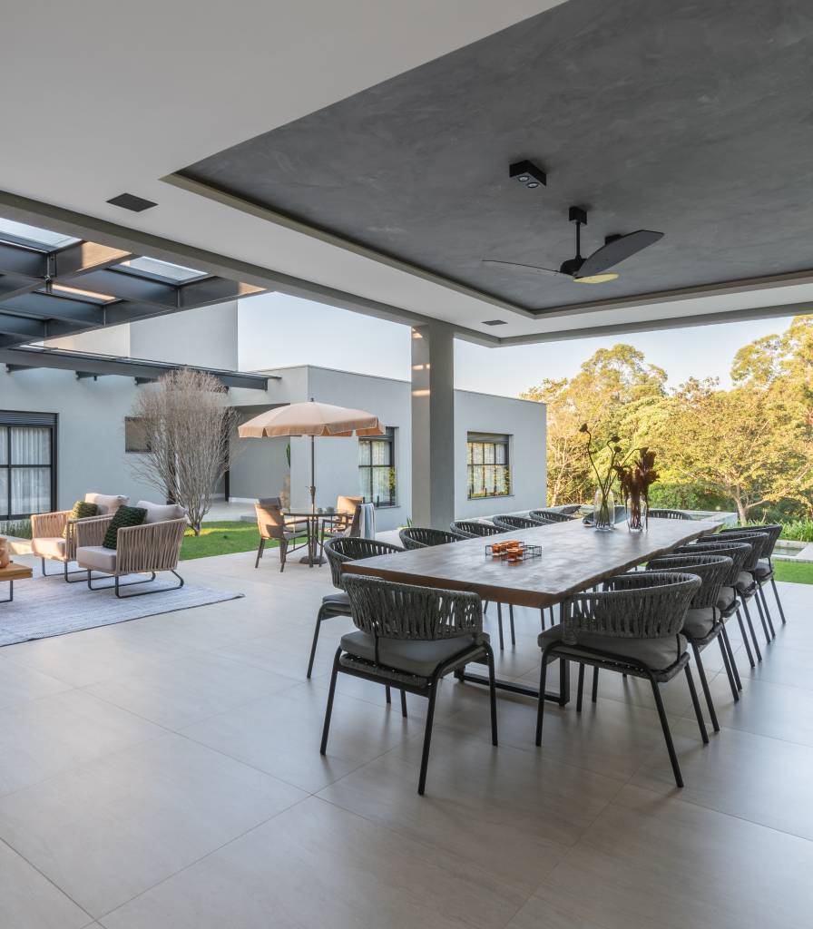 casa-interiores-sobrios-aberturas-assimetricas-fachada-27-area-gourmet Área gourmet com piso de porcelanato, mesa grande madeira e abertura para área externa.