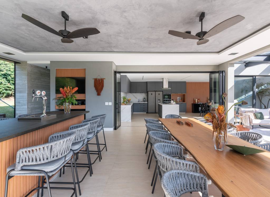 casa-interiores-sobrios-aberturas-assimetricas-fachada-28-area-gourmet Área gourmet com piso de porcelanato, mesa grande madeira e abertura para área externa.