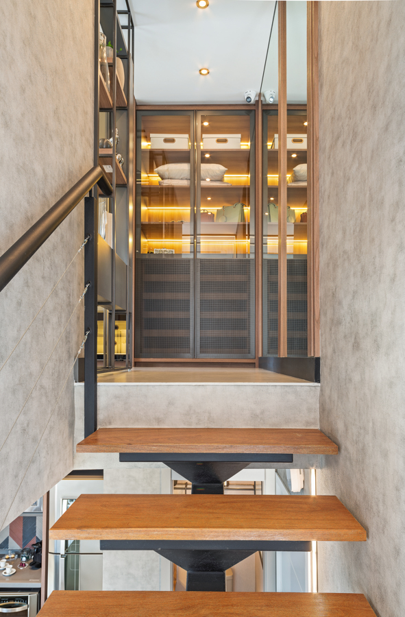 Duplex de 75 m² possui varanda com churrasqueira a carvão e suíte com closet. Na foto, closet com paredes de vidro e iluminação interna. Escada de acesso ao mezanino.