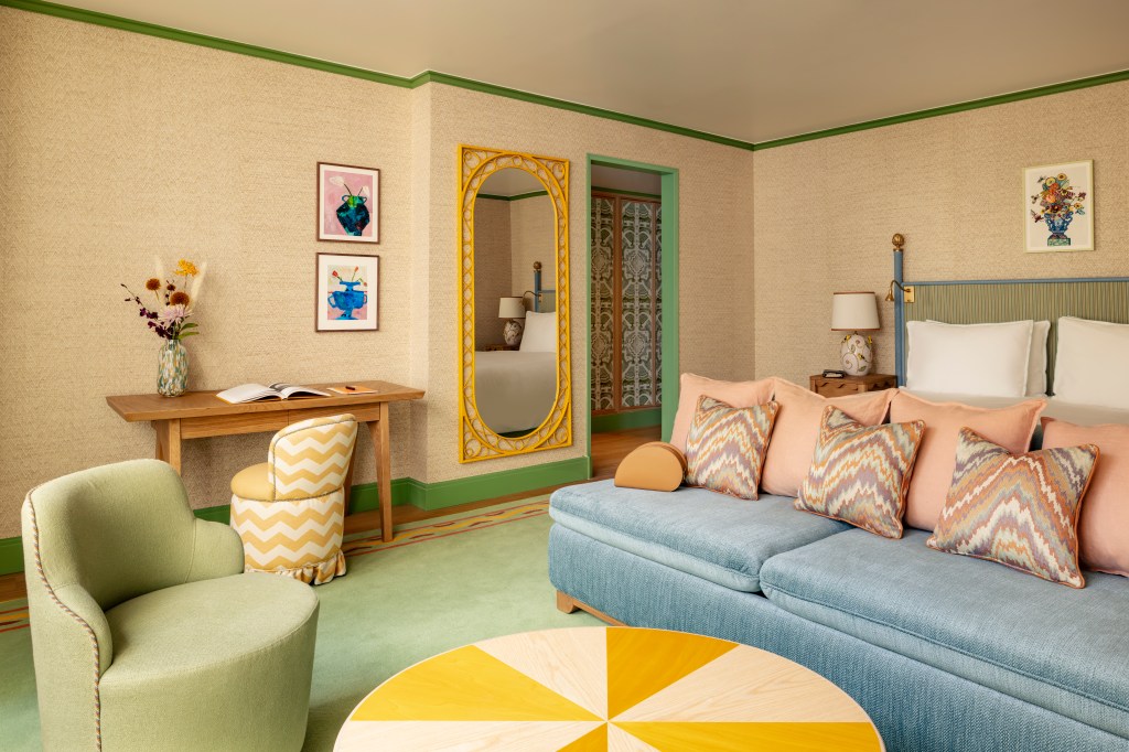 Quarto com piso verde, sofá azul e pufe branco e amarelo.