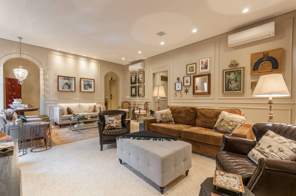 mesa-de-centro-tipos-em-alta-e-dicas-paiva-e-passarini-arquitetura-01 Sala de estar com decoração clássica, boiseries nas paredes, sofá marrom, poltronas de couro e pufe como mesa de centro.