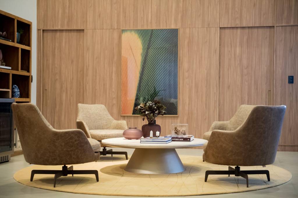 mesa-de-centro-tipos-em-alta-e-dicas-paiva-e-passarini-arquitetura-10 Sala de estar com poltronas beges, mesa de centro com tampo redondo e paredes revestidas de madeira.